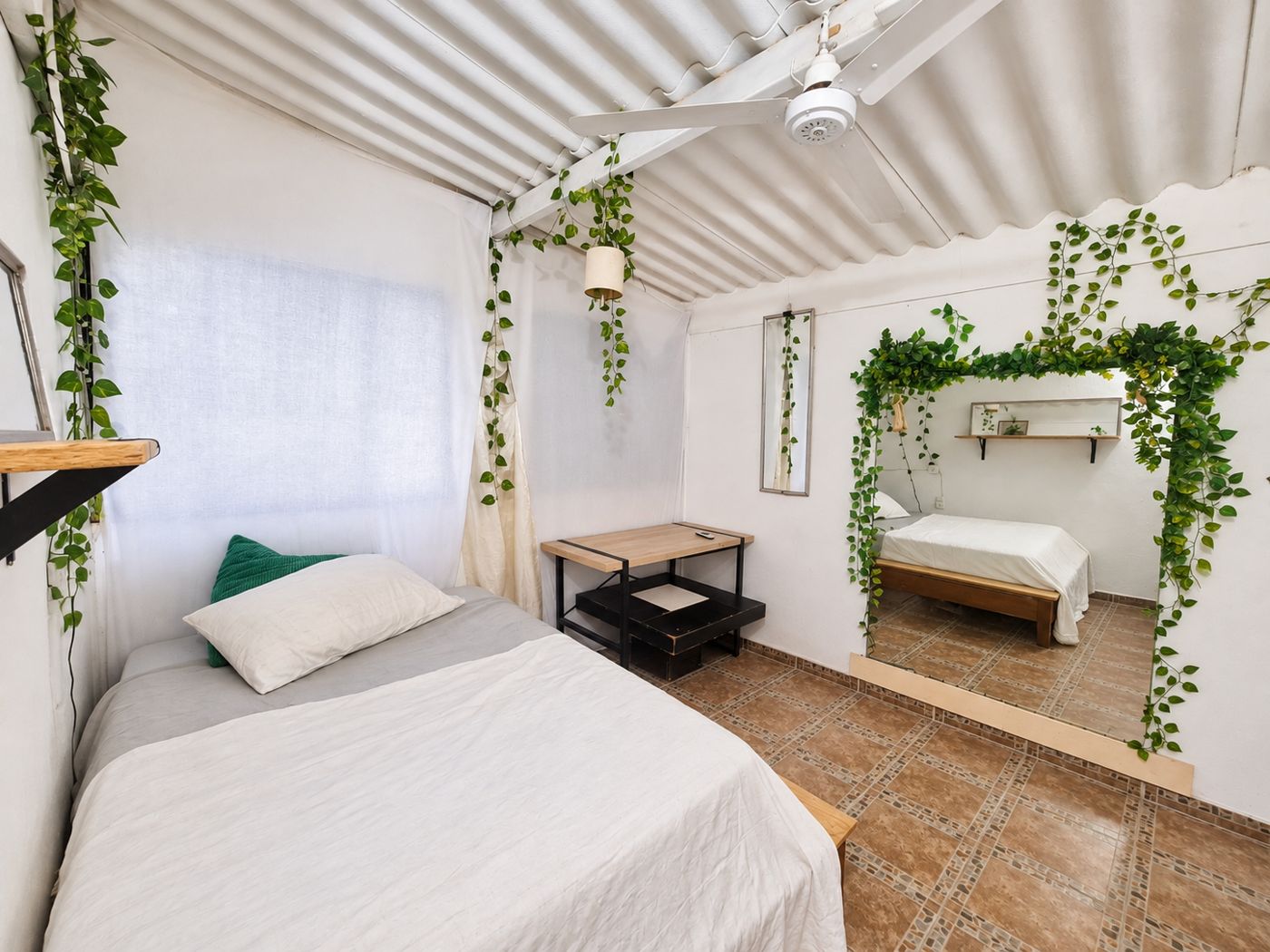Habitación amueblada con cama y espejo entre plantas